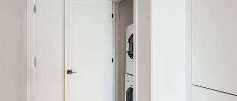 A laundry room with a washing machine and dryer, a white door, and a hallway.