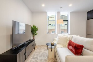 Ein modernes Wohnzimmer mit Flachbildfernseher, einer Couch, einem kleinen Tisch mit Kerze und einer Topfpflanze.