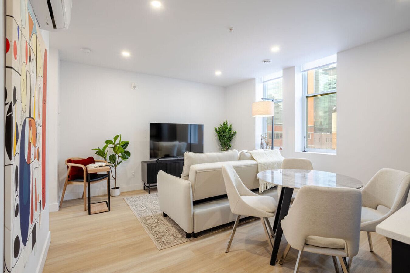 Uma sala de estar moderna com sofá, televisão, mesa de jantar com cadeiras e uma janela grande.