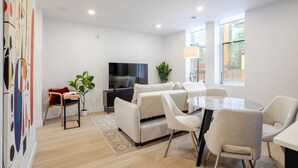 A modern living room with a sofa set, a TV, a dining table with chairs, and a large window. - Vintage Moderne – Old MTL Retreat (Montréal)