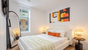 Ein Schlafzimmer mit einem Bett, zwei Nachttischen, einem Spiegel, einem Fenster und einem Wandbild.