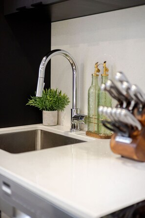 A kitchen sink with a modern faucet, a small potted plant, and decorative glass bottles. - Historic Hideaway – Bright Apartment in Old Montreal (Montréal)