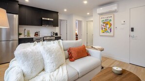 Ein modernes Wohnzimmer mit einem weißen Sofa, einer flauschigen weißen Decke und einem kleinen orangefarbenen Kissen.