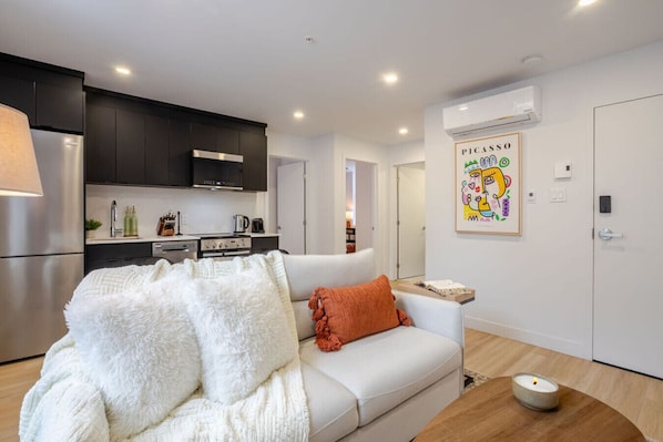Un salon moderne avec un canapé blanc, une couverture blanche moelleuse et un petit coussin orange.