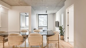 Ein modernes Interieur mit einem Esstisch, Stühlen, einem großen Fenster, einem Flachbildfernseher und einem Blumentopf.