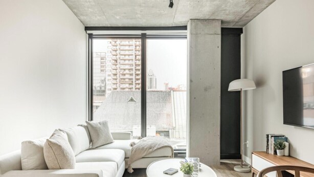 Un salon moderne avec un canapé blanc, une table basse, un lampadaire et un téléviseur fixé au mur.