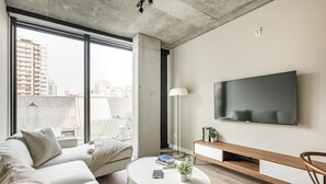Un salon moderne avec un canapé, une table basse, un téléviseur et une grande fenêtre donnant sur un paysage urbain.