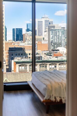 Ein Schlafzimmer mit einem großen Fenster mit Blick auf eine Stadtlandschaft.