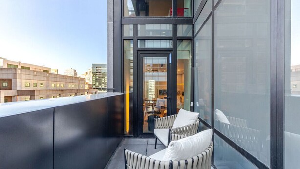 Un edificio moderno con un balcone dotato di due sedie in vimini e cuscini.