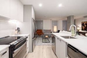 Una cuina moderna amb una illa central, una zona de menjador amb un sofà, i un saló amb una làmpada.