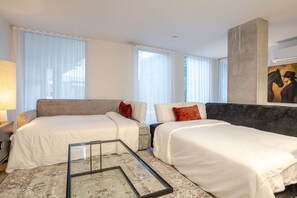 Habitació d'hotel amb dos llits, una taula de cafè de vidre i grans finestres amb cortines transparents.