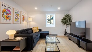 A modern living room with a sofa, a glass coffee table, a TV, and artwork on the wall. - Stylish Downtown Retreat (Montreal)