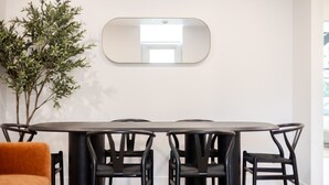 Een moderne eetruimte met een ronde tafel, vier stoelen, een tafel met glazen blad en een grote spiegel aan de muur.