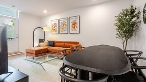 Een moderne woonkamer met een modulaire bank, een glazen salontafel, een eettafel met stoelen en drie ingelijste kunstwerken aan de wand.