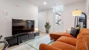 Een moderne woonkamer met een flatscreen televisie, een glazen salontafel, een bank en een lamp.