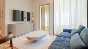 Un salon moderne avec un téléviseur à écran plat, une table basse ronde, un canapé et une grande fenêtre ornée de rideaux légers.