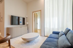 Un salon moderne avec un téléviseur à écran plat, une table basse ronde, un canapé et une grande fenêtre ornée de rideaux légers.