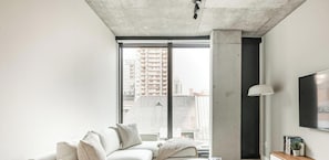 Ein modernes Wohnzimmer mit großem Fenster, einer Couch, einer Lampe und einem Fernseher.