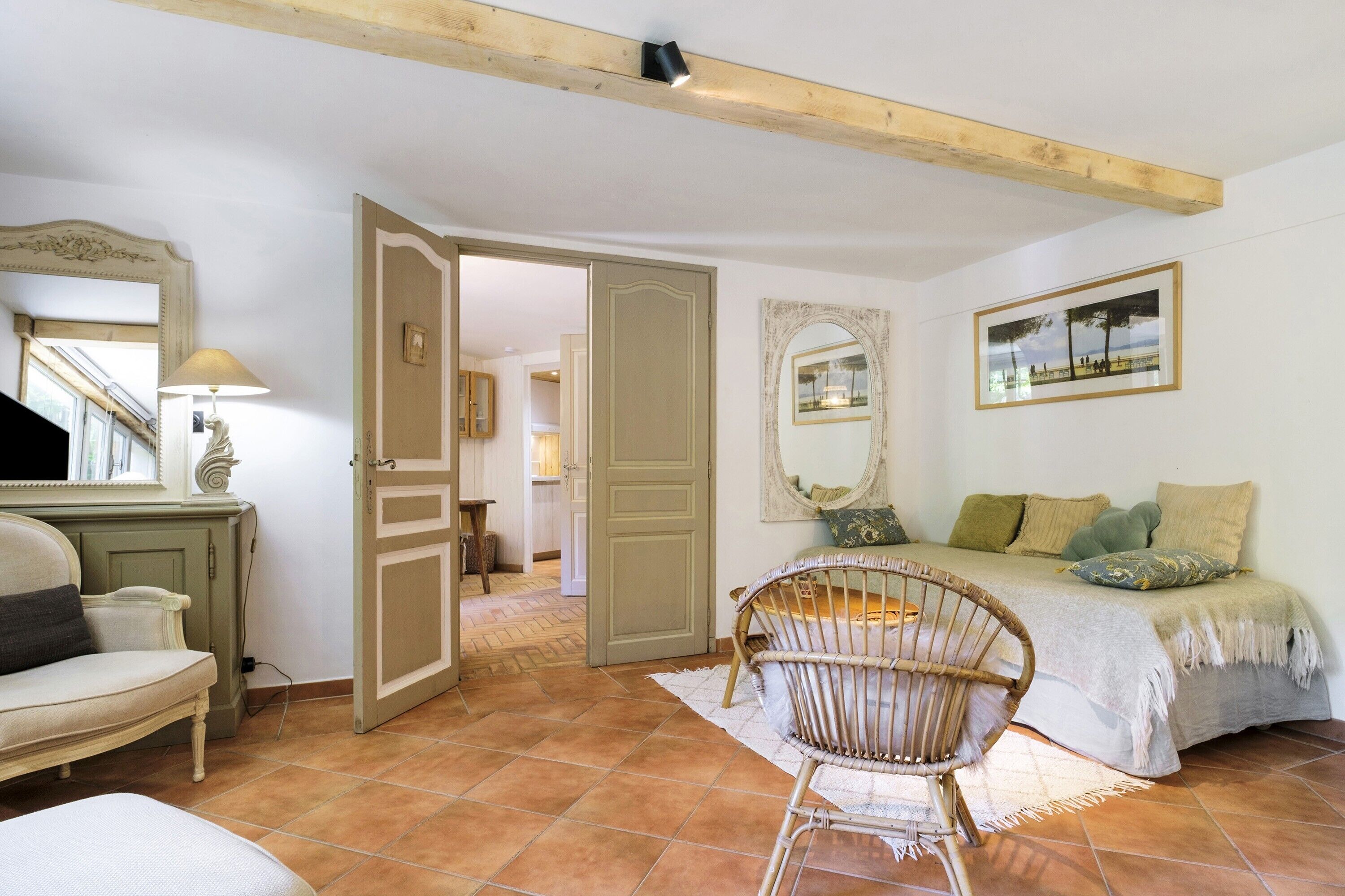 A bedroom with a bed, a chair, a mirror, and a door leading to another room.