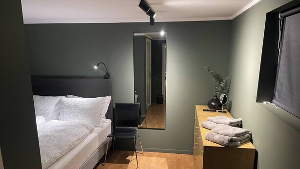 A bedroom with a bed, a chair, a desk with a mirror, and a window. - Renovated Apartment High Standard to City Center, Park (Tromsø)