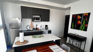 Una cocina moderna con armarios oscuros, una encimera blanca y un comedor con mesa y sillas de madera.