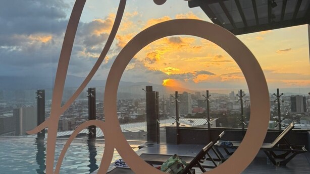Un área de piscina en la azotea con sillones de descanso y vistas al horizonte urbano al atardecer.