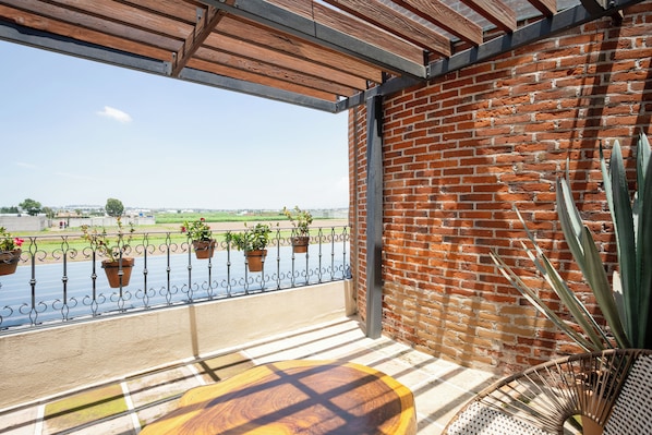 Un balcón con vista a un muro de ladrillo, plantas en macetas y una mesa de madera.