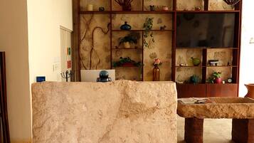 Una recepción con mostrador de piedra, un banco de madera y una estantería con plantas y objetos decorativos.
