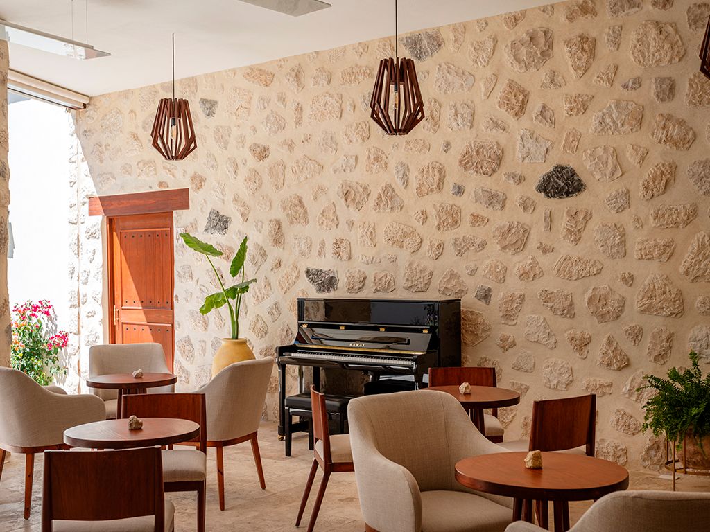 Una habitación con piano, pared de piedra y disposición de asientos.
