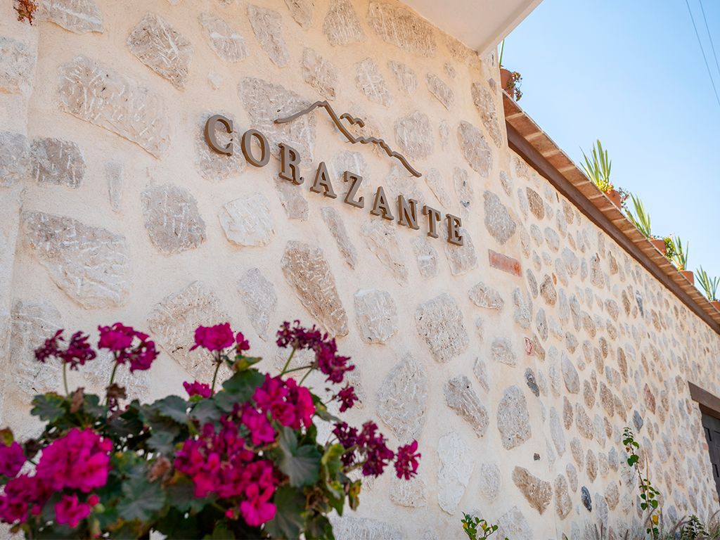 A stone wall with the name 'CORAZANTE' and some flowers in the foreground.