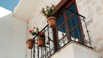 Un balcon orné de pots en terre cuite et de fleurs rouges, adossé à un immeuble à la façade en pierre.