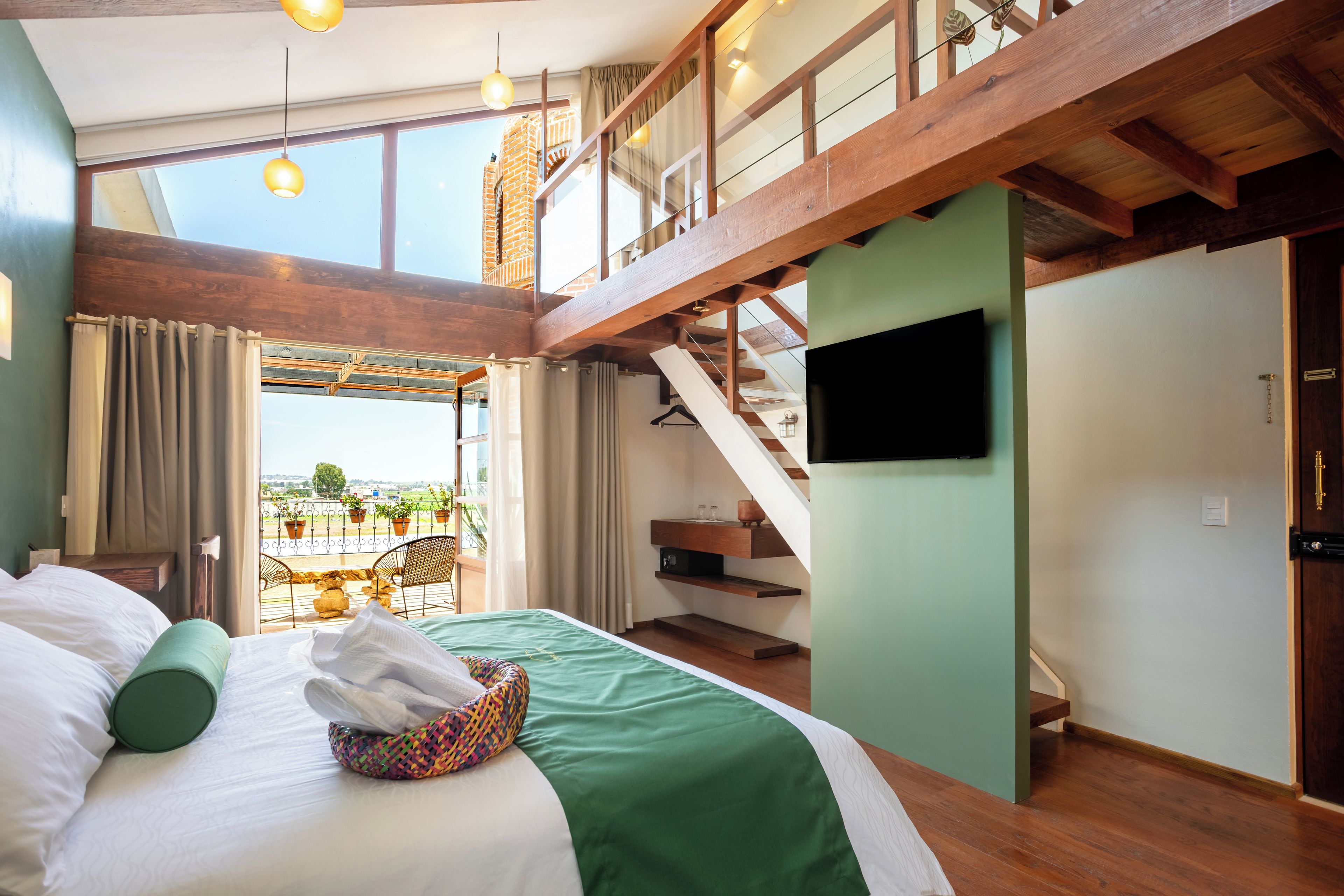 A hotel room with a bed, a TV, a balcony with potted plants, and a staircase.