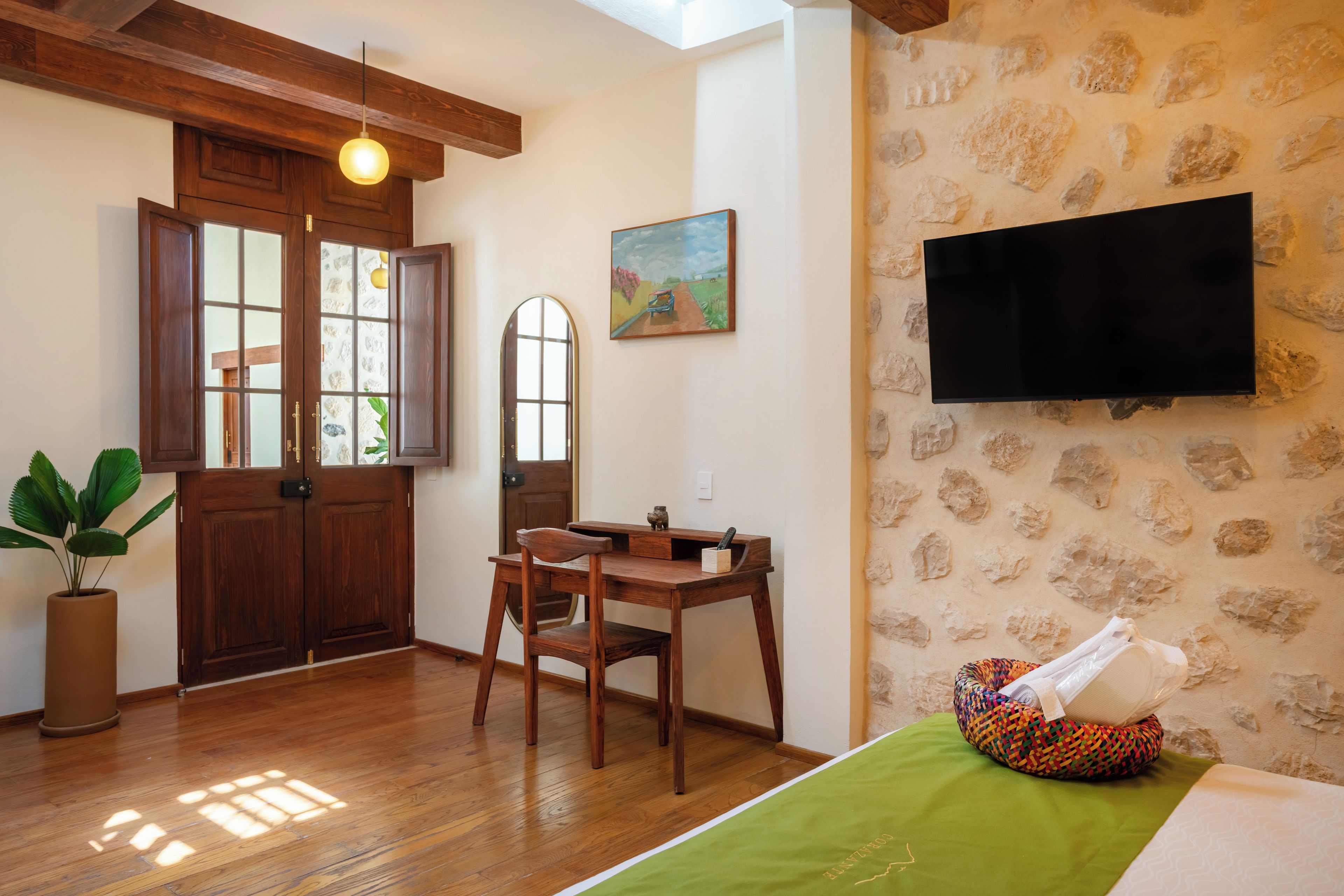 Una habitación con puerta de madera, una mesa con silla, una planta en maceta, un cuadro en la pared y un televisor de pantalla plana montado sobre una pared con textura.