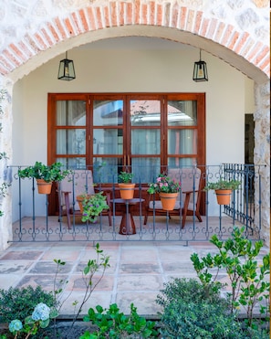 Une terrasse extérieure avec une table et des chaises, entourée de plantes en pot et dotée d’un sol carrelé en pierre.