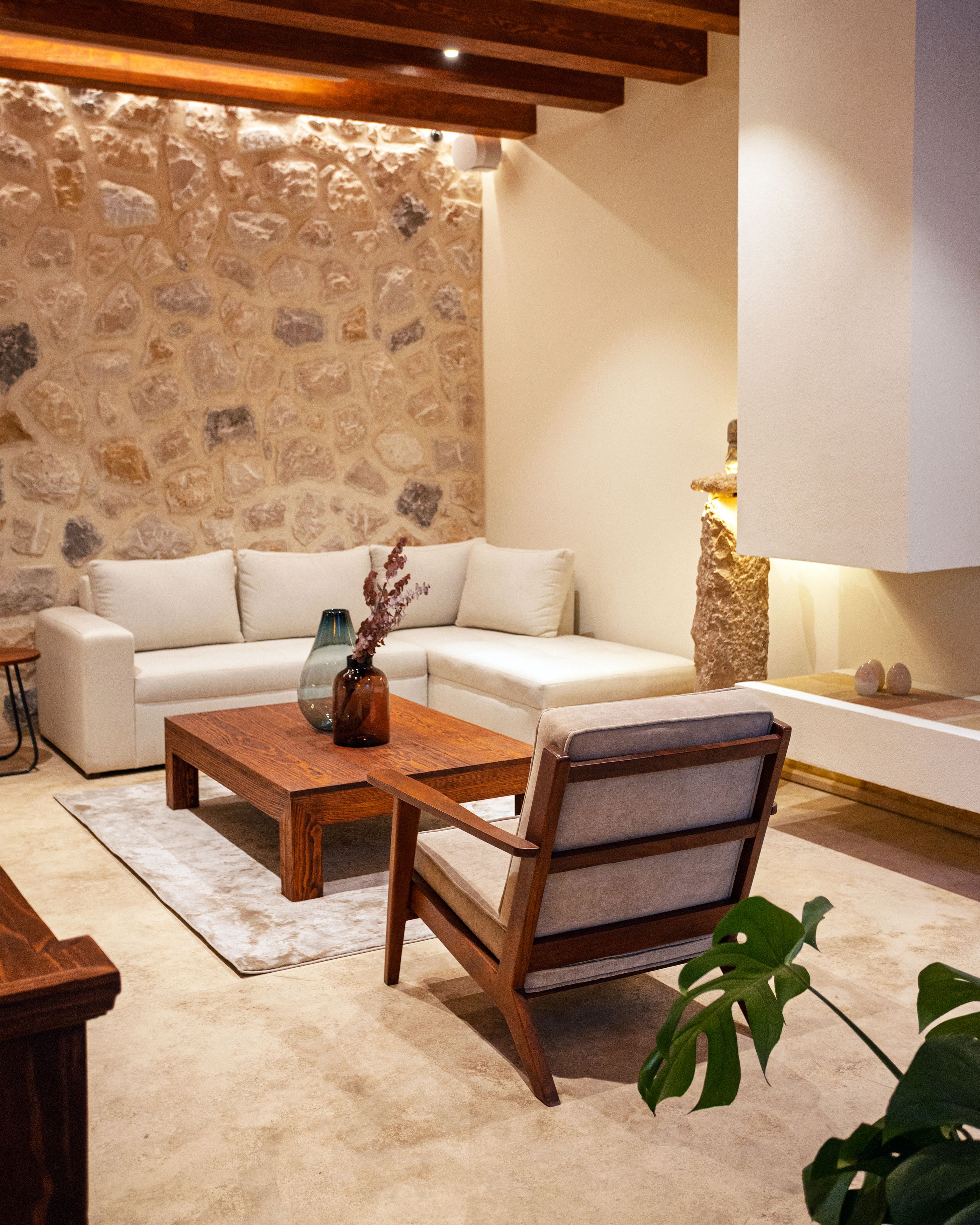 Una sala de estar moderna con una pared de piedra, un sofá blanco, una mesa de centro de madera y una planta.