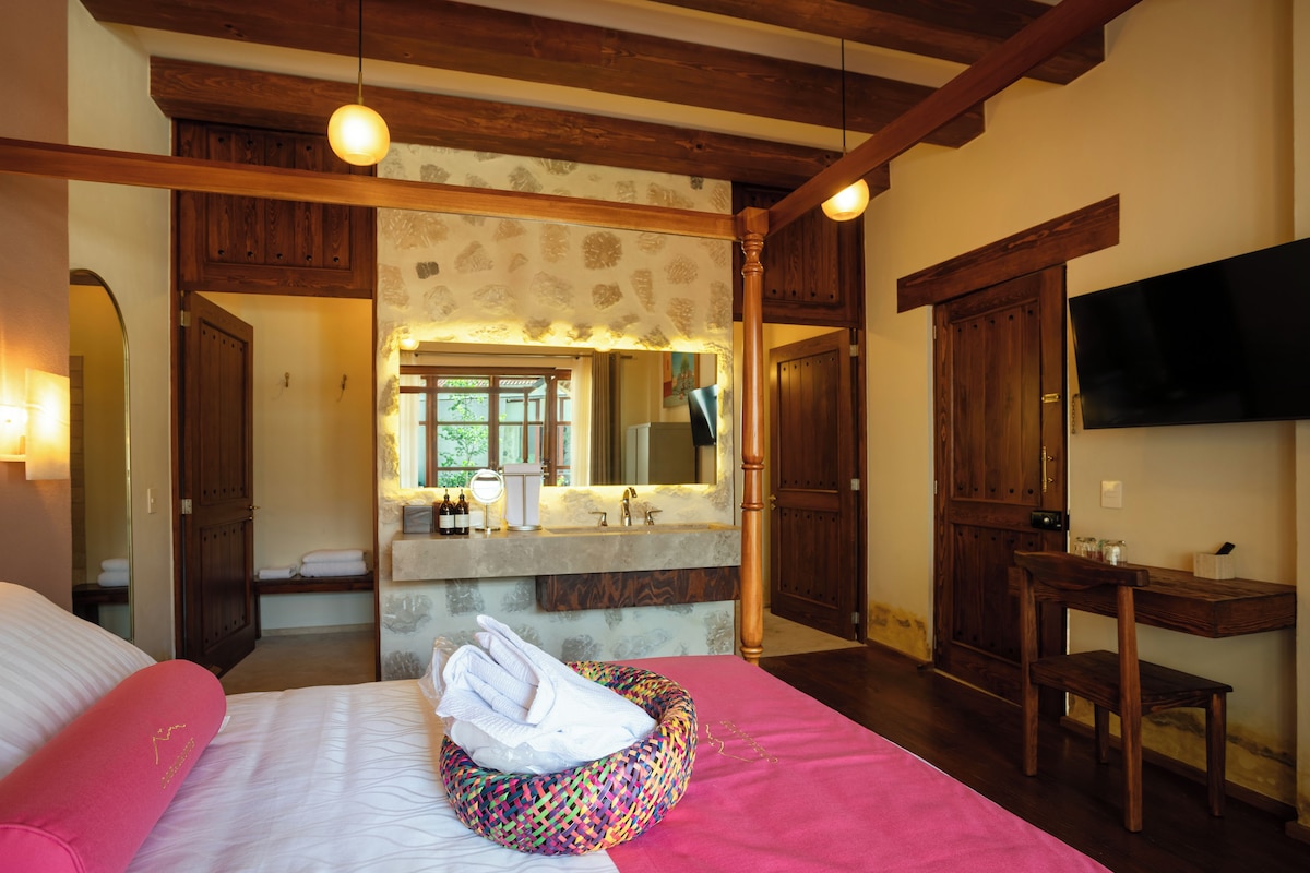 Quarto de hotel com cama, banheiro com espelho, pia e televisão na parede.