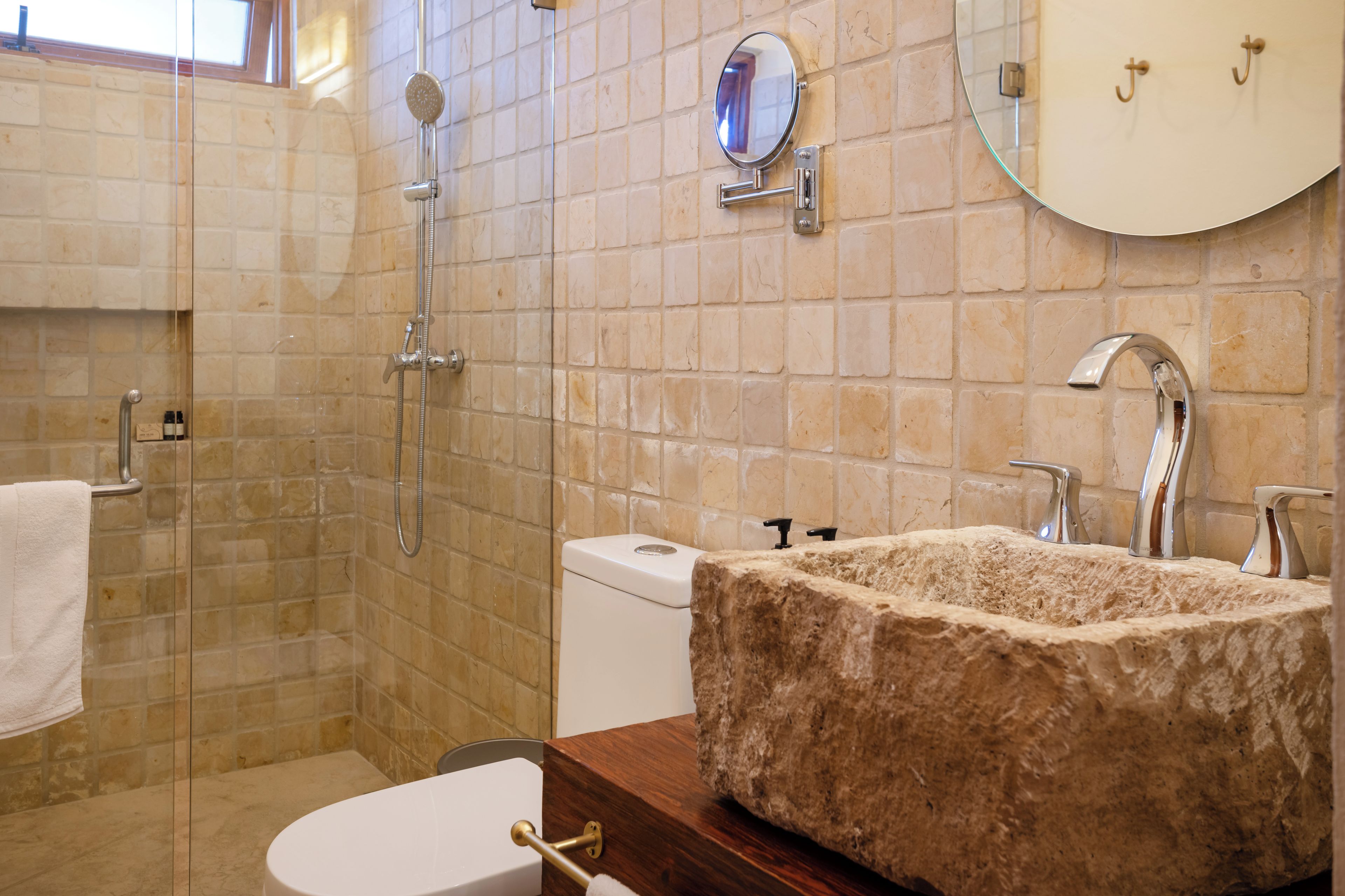 A bathroom with a stone sink, a toilet, a shower, and a mirror on the wall.