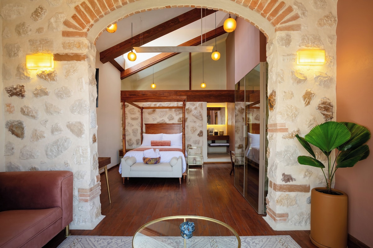 A hotel room with a stone wall, a bed, a sitting area, and a large potted plant.