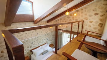 Un dormitorio con techo de madera, una cama con ropa blanca, una mesita de noche y una ventana con vista al cielo.