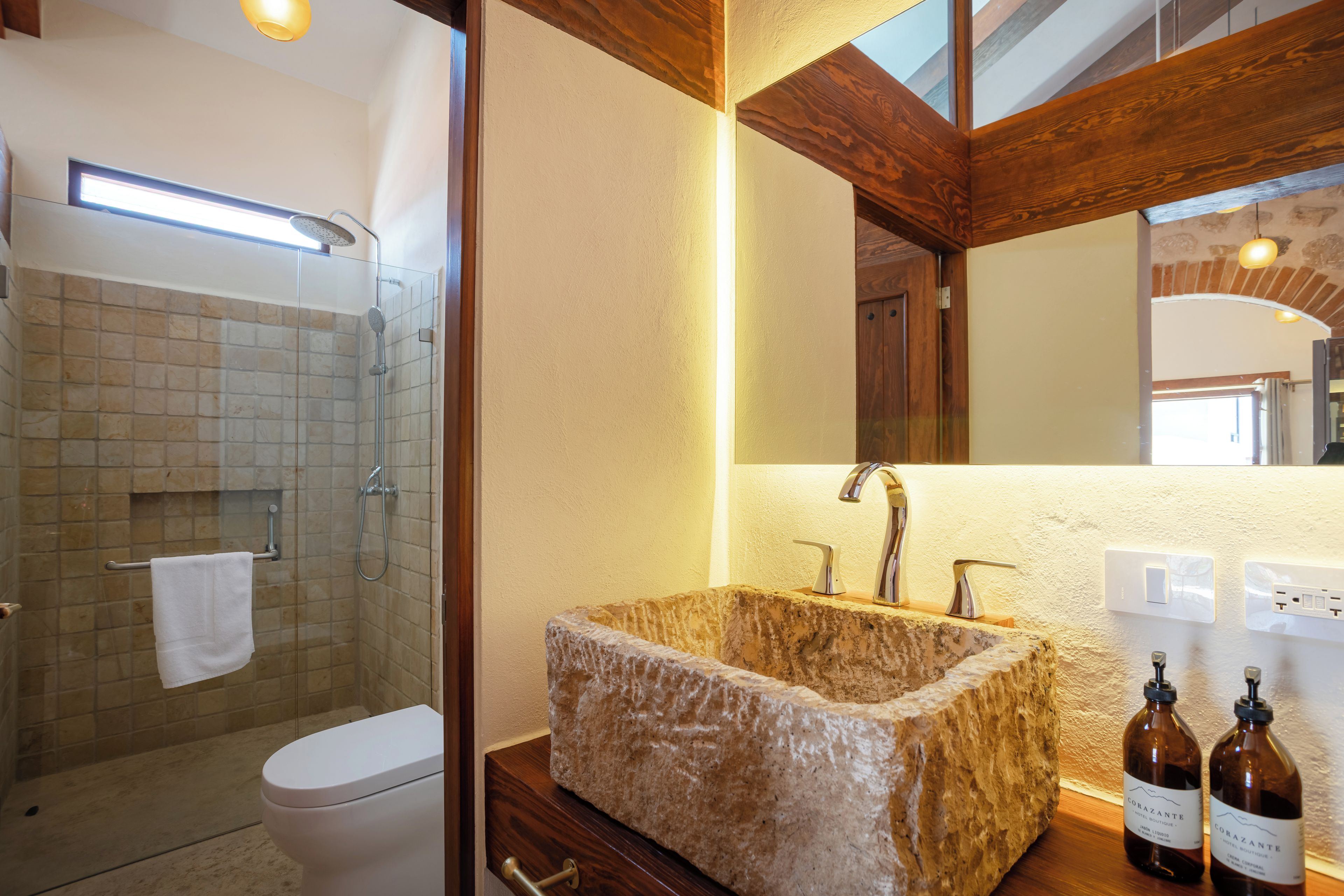 Un baño con cabina de ducha de vidrio, inodoro blanco, lavabo de piedra y tocador de madera.