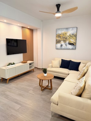 A modern living room with a flat-screen TV, a ceiling fan, a sofa, a coffee table, and a wall-mounted artwork.