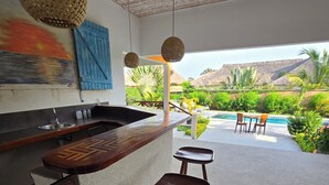 Eine Bar mit Hockern, einer Theke und Blick auf Pool und Grünanlage.