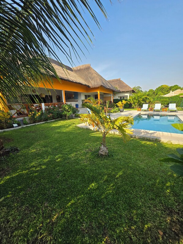 A resort with a swimming pool, thatched-roof buildings, and a well-maintained lawn.