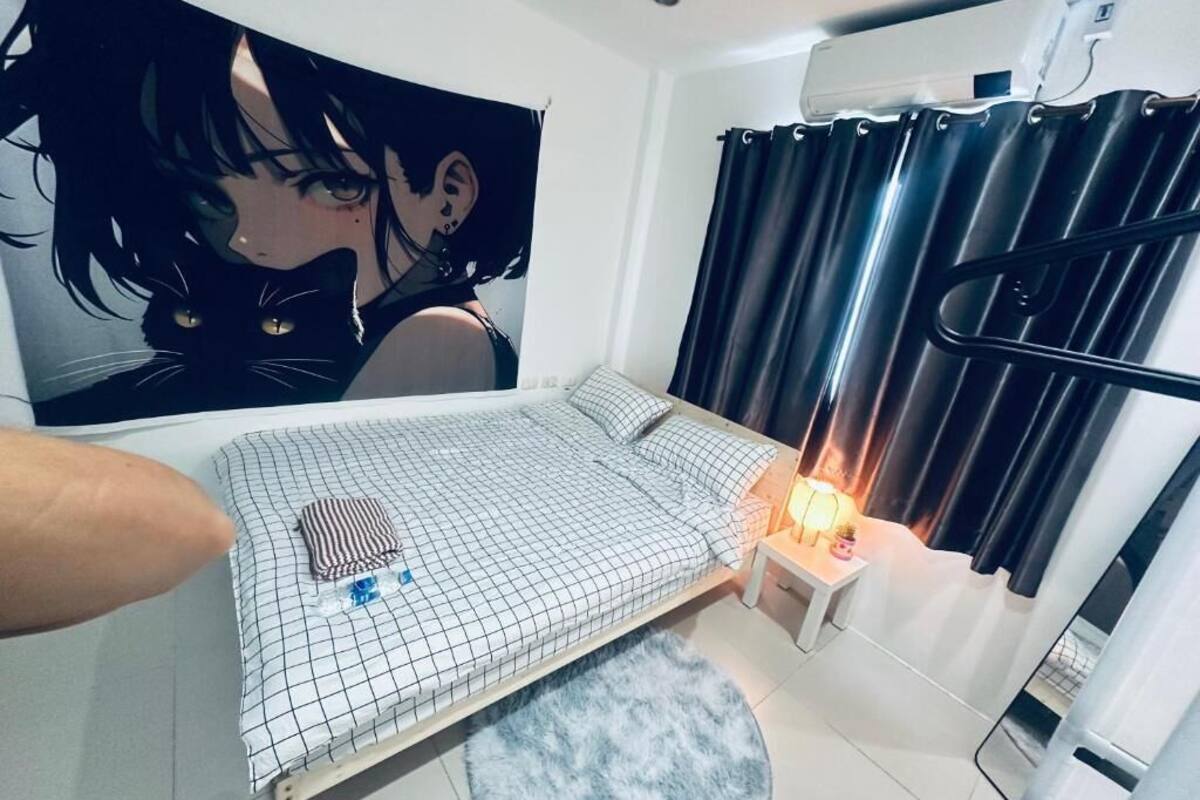 A bedroom with a bed, a nightstand, a lamp, a window with curtains, and a wall tapestry.