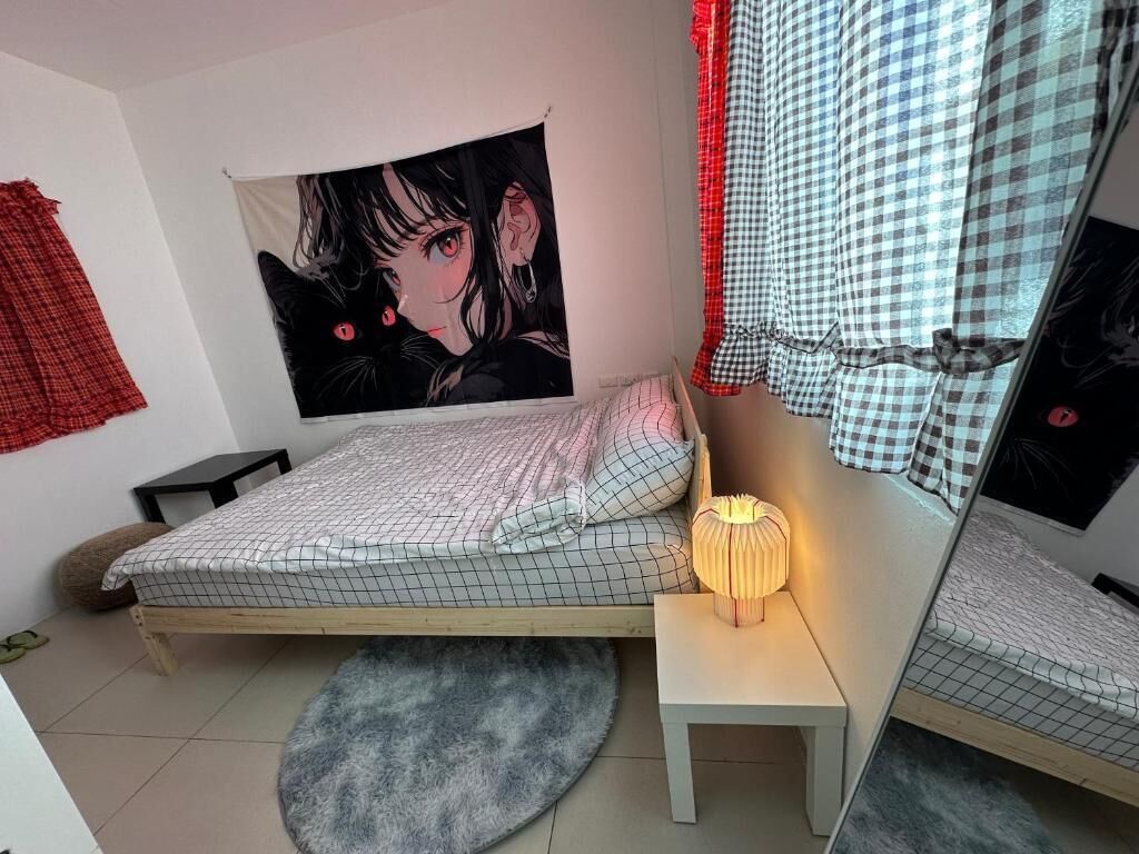 A bedroom with a bed, a bedside lamp, a round rug, a wall tapestry, and a checkered curtain.