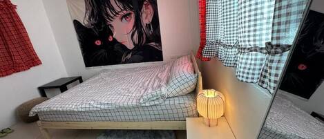 A bedroom with a bed, a bedside lamp, a round rug, a wall tapestry, and a checkered curtain.