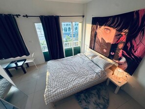 Un dormitorio con cama, escritorio, silla, ventana con cortinas y un cartel grande en la pared.