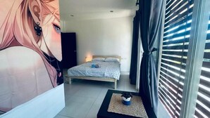 A bedroom with a bed, a small table with a plant, a wall with a large poster, and a window with blinds. - HulaFling Homestay  (Sa Khu)