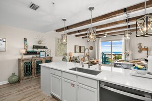 Une cuisine dotée d’un grand îlot central, de poutres en bois, de luminaires suspendus et offrant une vue sur l’extérieur.