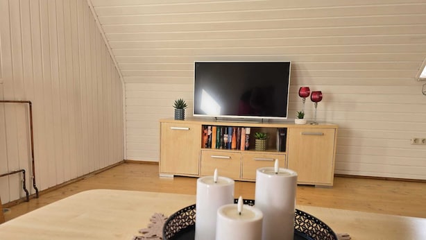 Una habitación con una televisión sobre un mueble de madera, una bandeja redonda negra con velas y una alfombra estampada.